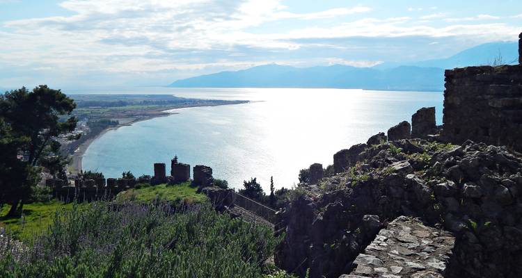 Des murs de pierre encadrent un vaste paysage urbain côtier et le golfe scintillant en contrebas.