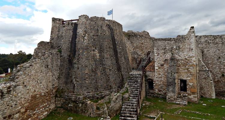 Massif donjon de pierre de château médiéval s'élève sous un parapet surmonté de drapeaux.