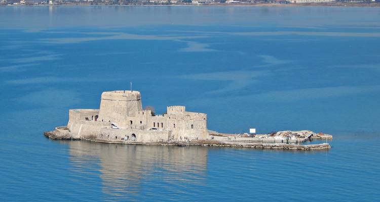 Une petite forteresse en pierre se dresse sur un îlot entouré par les eaux calmes et bleues de la mer.