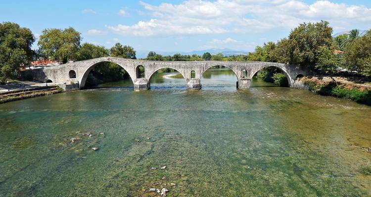 Pont historique en pierre à arches multiples enjambe une rivière claire et peu profonde.