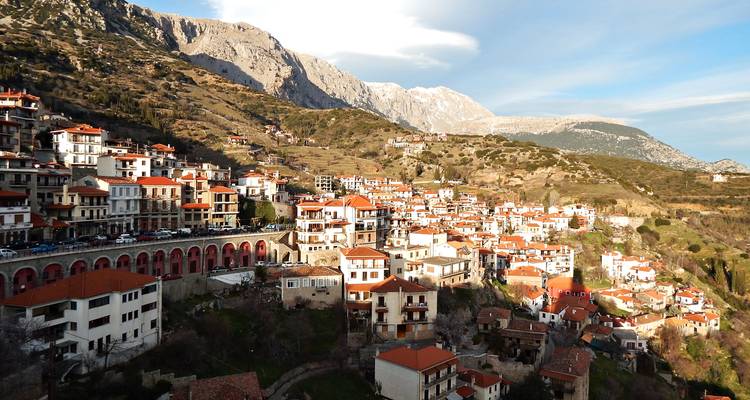 Une ville de montagne aux maisons à toits rouges se trouve au pied de pics escarpés saupoudrés de neige.