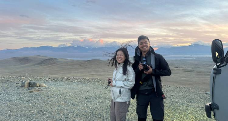 Dos personas con cámaras sonriendo ante un paisaje pintoresco durante la puesta del sol.