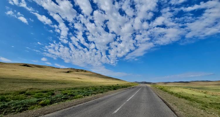 Carretera abierta que atraviesa un paisaje bajo un cielo azul con nubes dispersas.