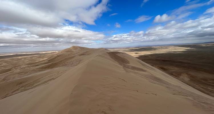 Alta duna de arena con una mezcla de cielo azul y nubes.