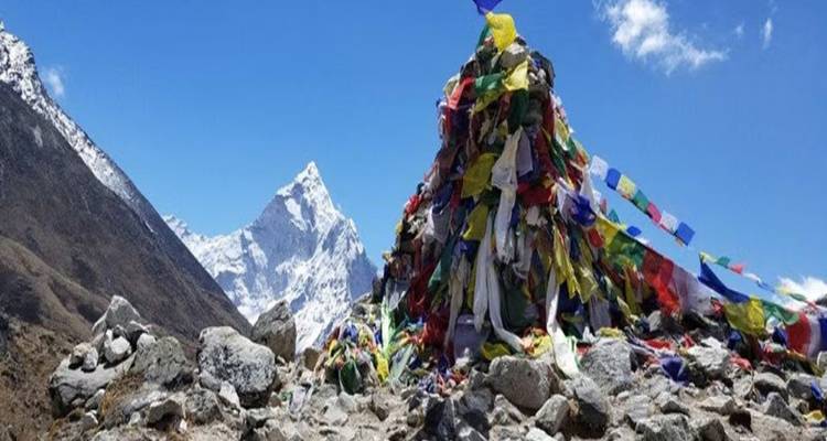 Drapeaux de prière colorés sur une montagne avec des sommets enneigés en arrière-plan.
