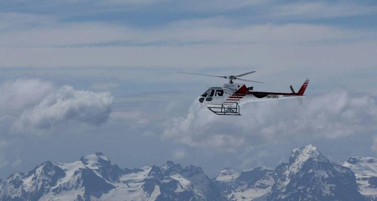 Hélicoptère volant haut avec des montagnes enneigées en dessous.