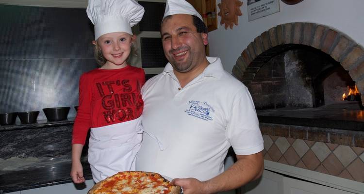 Enfant et chef cuisinier tenant une pizza dans une cuisine.