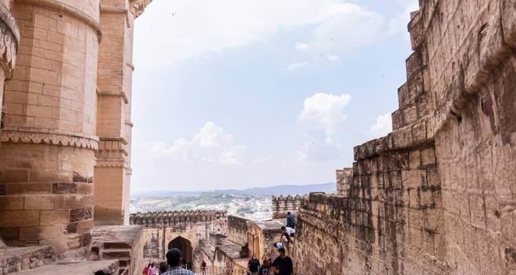 Des touristes marchant le long d'un mur de forteresse historique avec une vue sur la ville.