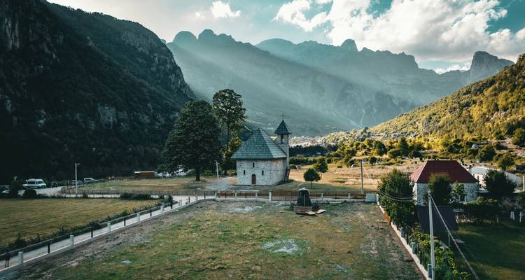 Une église dans une vallée montagneuse avec la lumière du soleil qui filtre par-dessus les sommets.