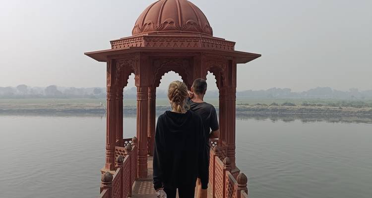 Dos personas paradas en un pabellón rojo con vista a un río tranquilo.