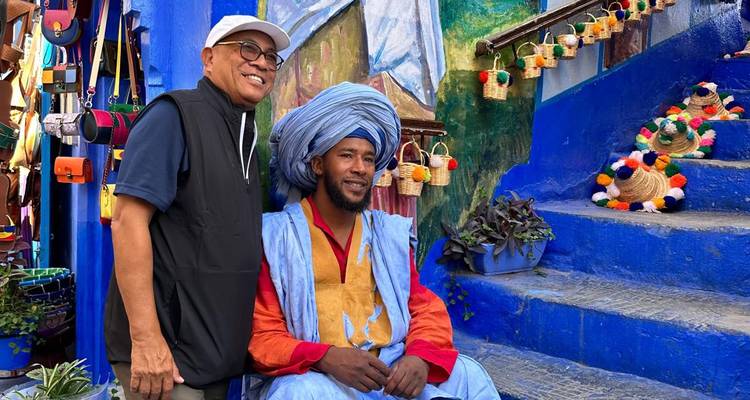 Zwei Männer posieren in einer lebendigen blauen Straße mit buntem Kunsthandwerk in Chefchaouen.