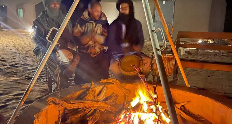Menschen sitzen nachts um ein Lagerfeuer und spielen Trommeln.