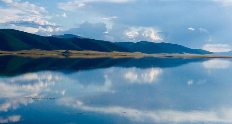 Beau lac avec un arrière-plan montagneux et un ciel clair se reflétant sur l'eau.