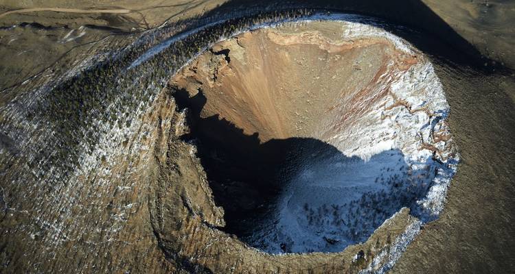 Vue aérienne d'un cratère volcanique avec neige et ombres.