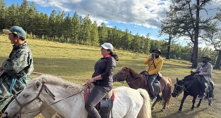 Personas montando caballos en un sendero arbolado.