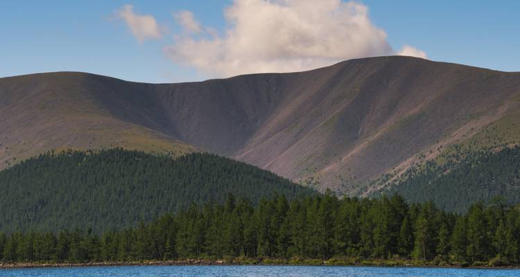 Lago con bosque circundante y montañas bajo un cielo despejado.
