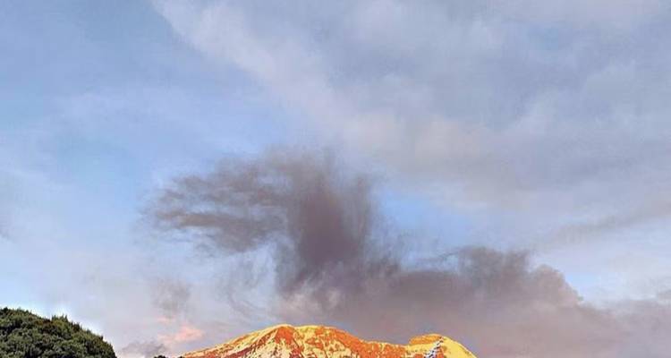 Sonnenbeschienener schneebedeckter Berggipfel unter bunten Wolken.