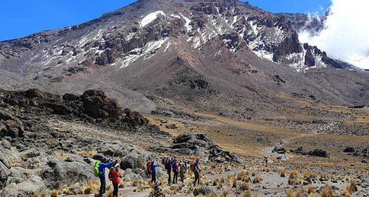 Excursionistas en un paisaje rocoso con una montaña cubierta de nieve.