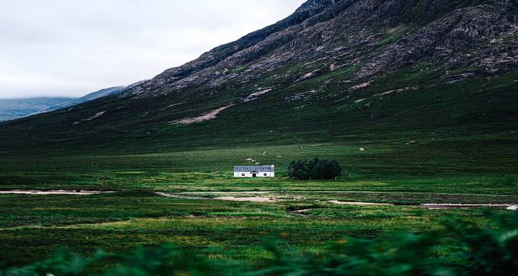 Isolated house in a vast green valley under a mountain.