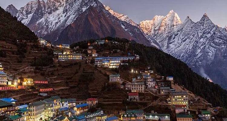 Town nestled at the base of snow-capped mountains at dusk.