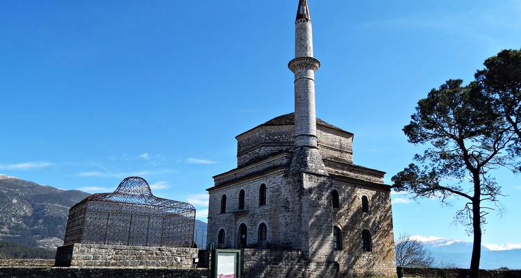 Mezquita histórica de Fethiye con minarete alto junto al lago Pamvotis respaldada por montañas con picos nevados.