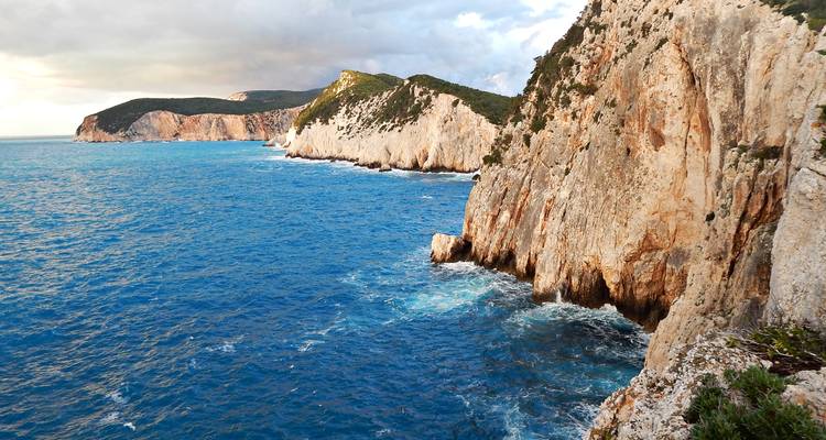Des falaises blanches spectaculaires plongent dans la mer Ionienne d'un bleu vibrant avec des vagues qui se brisent à leur base.
