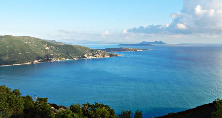 Vue panoramique côtière de collines émeraude rencontrant une vaste mer bleue et des îles lointaines sous un ciel dégagé.