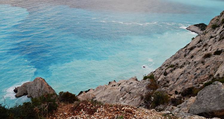 Point de vue élevé donnant sur des eaux turquoise translucides et un rivage rocheux en contrebas de pentes abruptes.