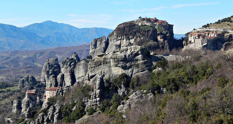 Spectaculaires piliers de roche de Météora surmontés de monastères anciens au milieu de montagnes lointaines.