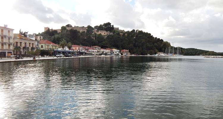 Griekse kustplaats met kleurrijke gebouwen aan de waterkant en een kleine heuveltopvesting weerspiegeld in het kalme havenwater