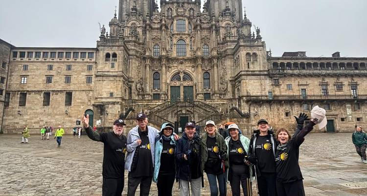 Peregrinos celebrando la llegada frente a la catedral de Santiago de Compostela en una plaza lluviosa