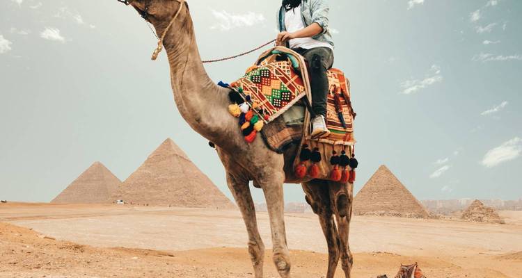 Voyageur chevauchant un chameau devant les pyramides par une belle journée désertique