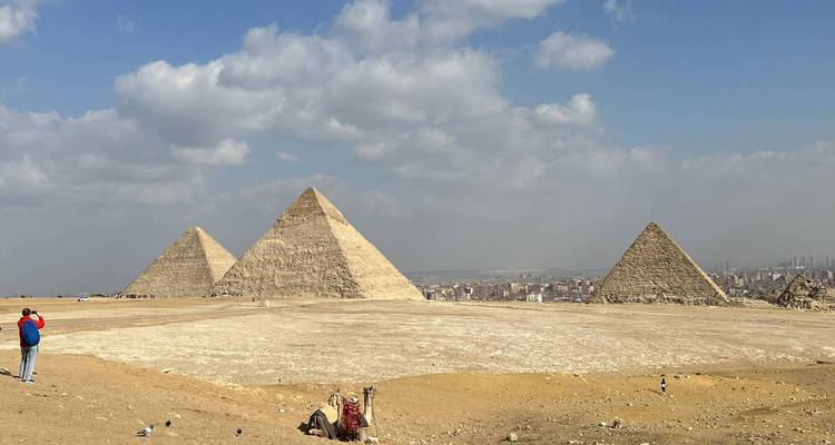 Large panorama du complexe des pyramides de Giza avec un visiteur solitaire prenant des photos
