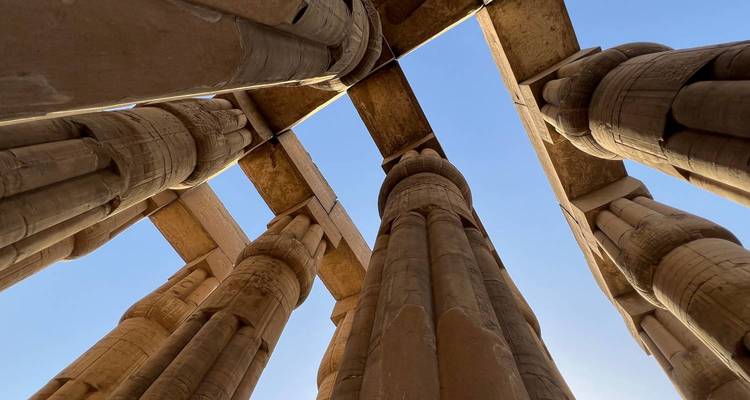Vue ascendante entre d'énormes colonnes de grès d'un ancien temple égyptien sur fond de ciel bleu