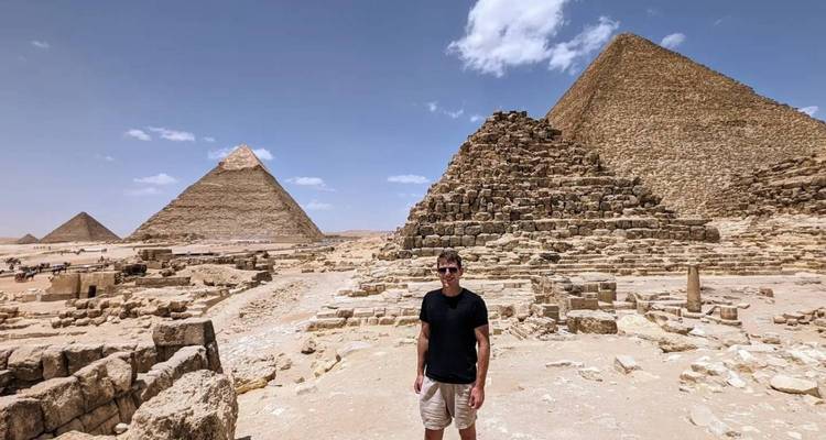 Visiteur souriant se tenant parmi des blocs de pierre anciens avec les pyramides s'élevant derrière