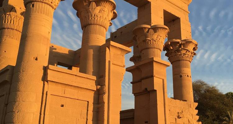 Colonnes de temple égyptien illuminées d'or avec un ciel rayé dramatique au coucher du soleil