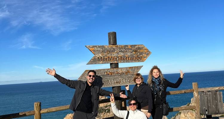 Group of people posing beside a wooden sign pointing towards seas.