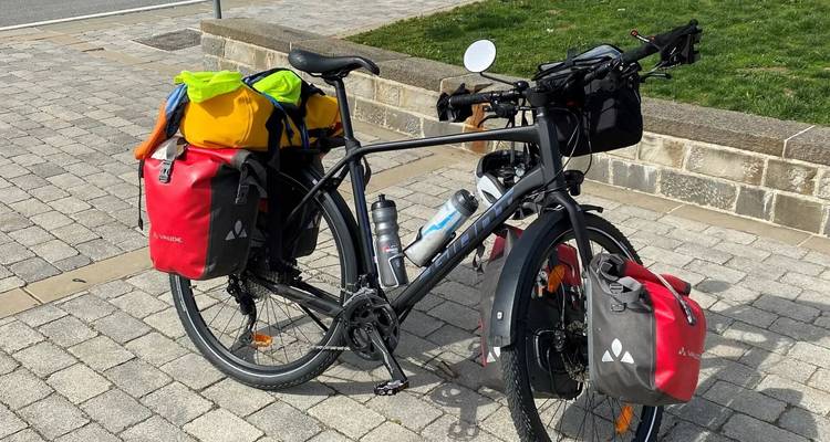 Bicicleta equipada para viajar con bolsas, estacionada en una calle empedrada.