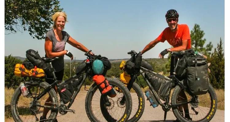Two cyclists with loaded bicycles on a sunny day, smiling at the camera.