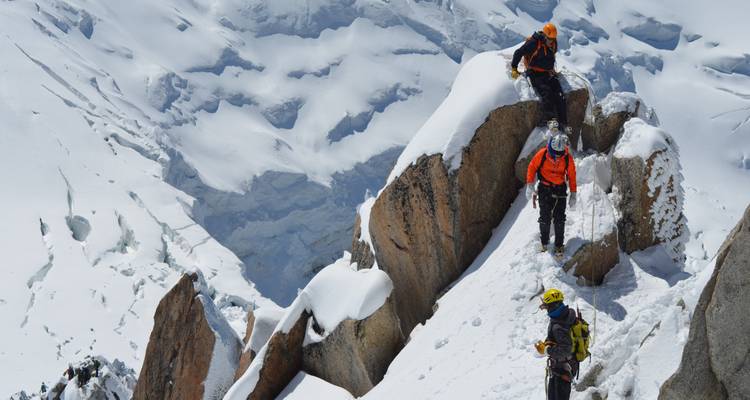 Escaladores atravesando una cresta nevada con montañas al fondo.
