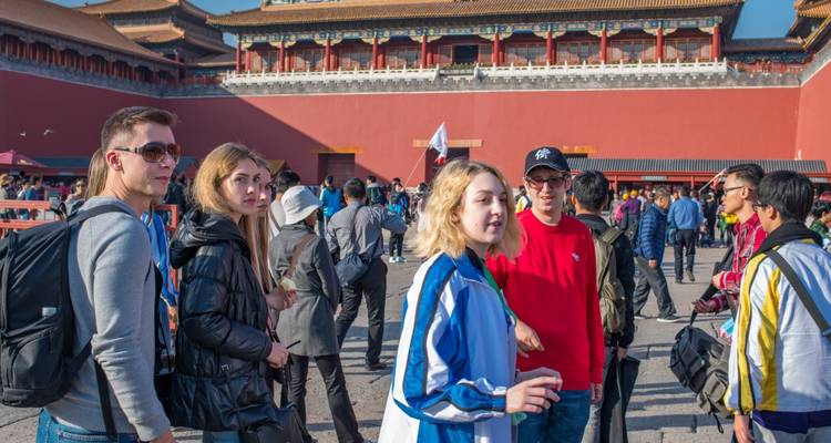 Groupe de touristes debout devant une structure aux murs rouges, possiblement la Cité interdite.