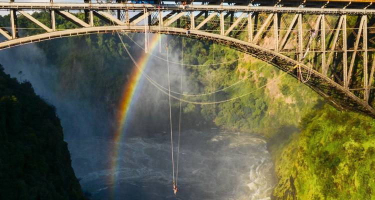 Person beim Bungee-Springen von einer Brücke mit Regenbogen im Hintergrund.