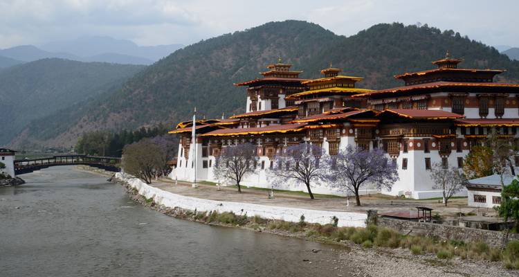 Fortaleza tradicional butanesa junto a un río con un fondo montañoso.