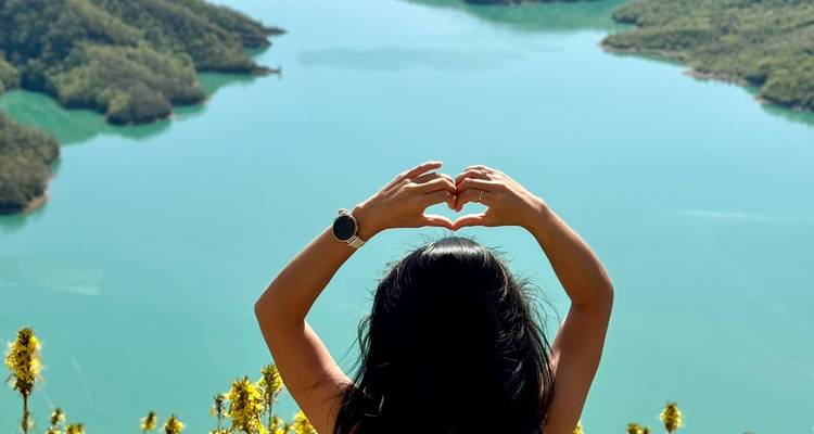 Mujer formando un corazón con las manos mirando hacia un lago turquesa.