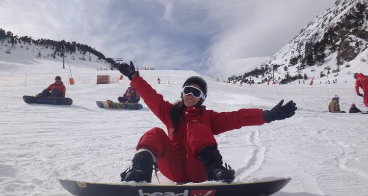 Woman smiling while snowboarding with mountains in the background.
