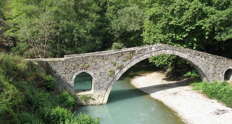 Stone bridge over a river surrounded by greenery.