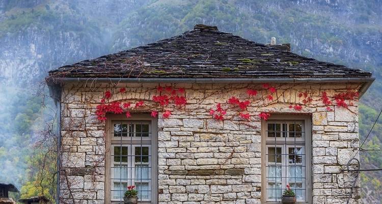Stone building with red vines and a mountain backdrop.