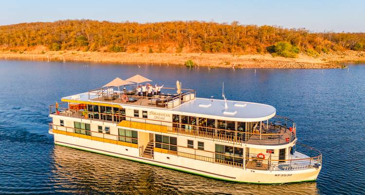 Lujoso barco de crucero fluvial blanco deslizándose sobre aguas tranquilas con orilla boscosa al atardecer