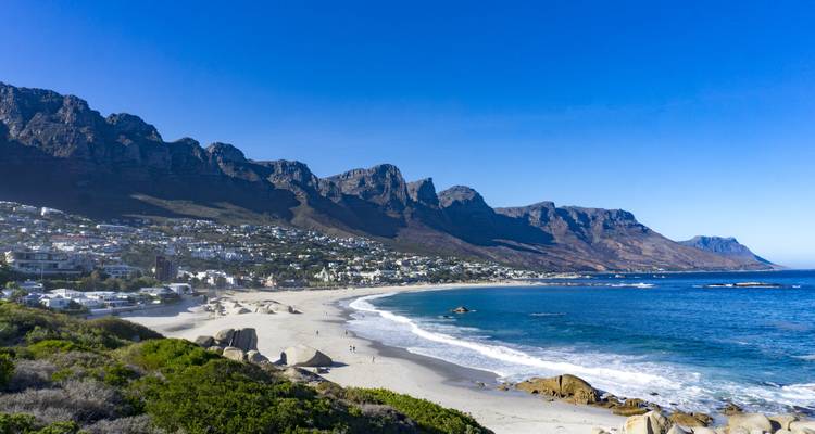 Amplia playa de arena de Camps Bay respaldada por la imponente cordillera de los Doce Apóstoles y un océano azul vibrante.
