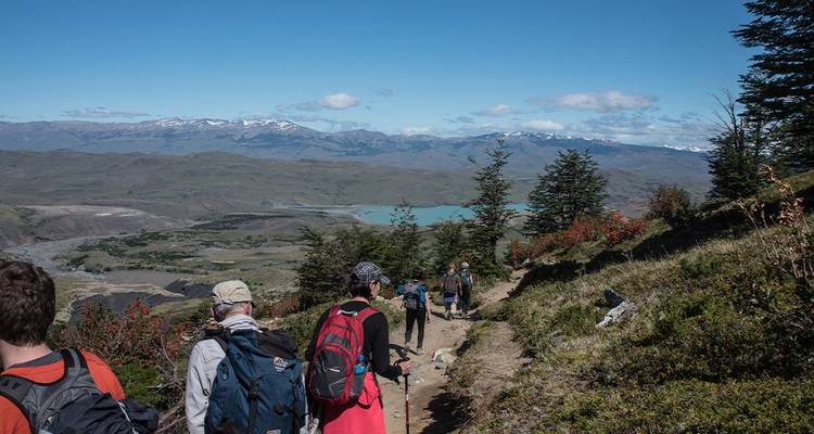 Excursionistas en un sendero con vista a un lago en terreno montañoso.